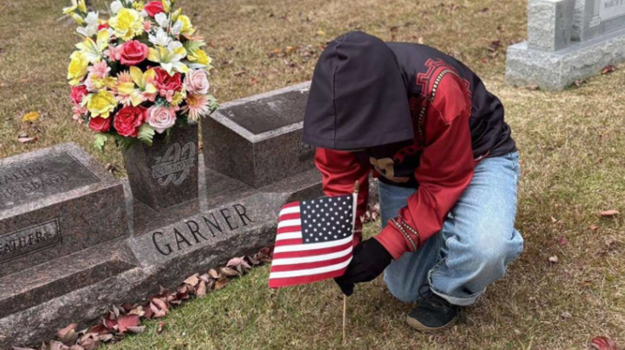 Boy places flag in ground next to grave
